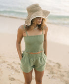 Woman wearing smocked tube top with spaghetti straps and short in medium green linen.