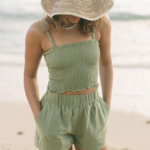 Woman wearing smocked tube top with spaghetti straps and short in medium green linen.
