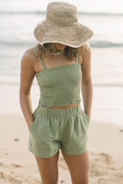 Woman wearing smocked tube top with spaghetti straps and short in medium green linen.