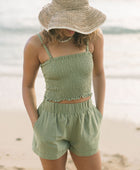 Woman wearing smocked tube top with spaghetti straps and short in medium green linen.