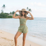 Woman wearing smocked tube top with spaghetti straps and short in medium green linen.