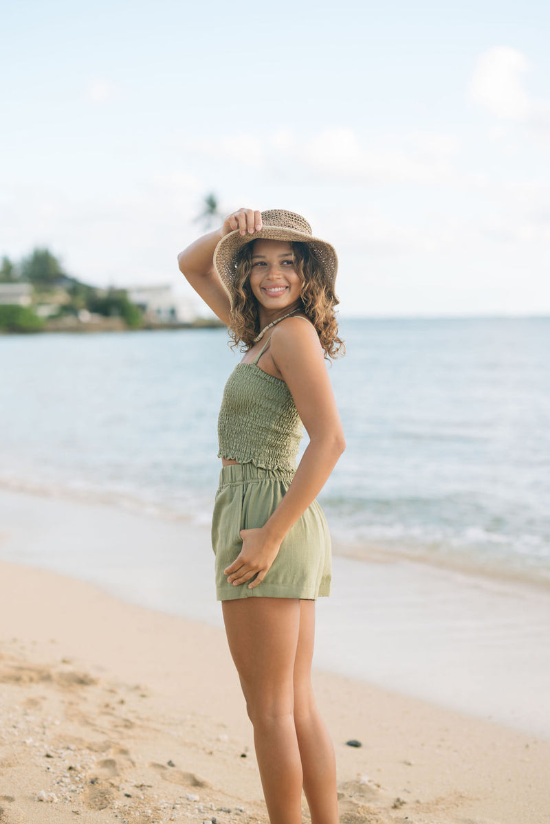 Woman wearing smocked tube top with spaghetti straps and short in medium green linen.