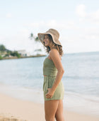 Woman wearing smocked tube top with spaghetti straps and short in medium green linen.