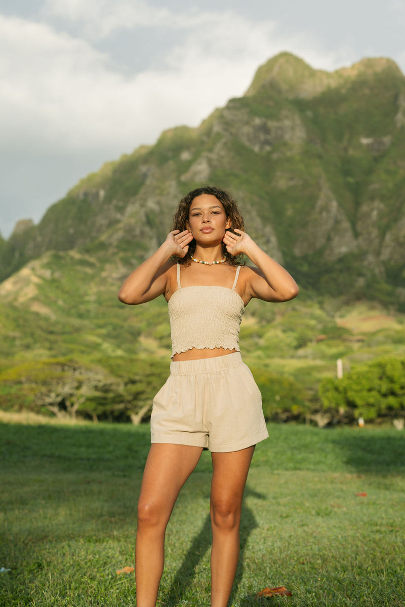 Woman wearing smocked beige linen tube top with spaghetti straps and short.