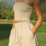 Woman wearing smocked beige linen tube top with spaghetti straps and short.