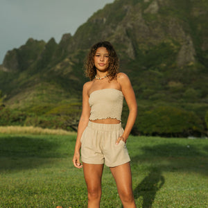 Woman wearing smocked beige linen tube top with spaghetti straps and shorts.