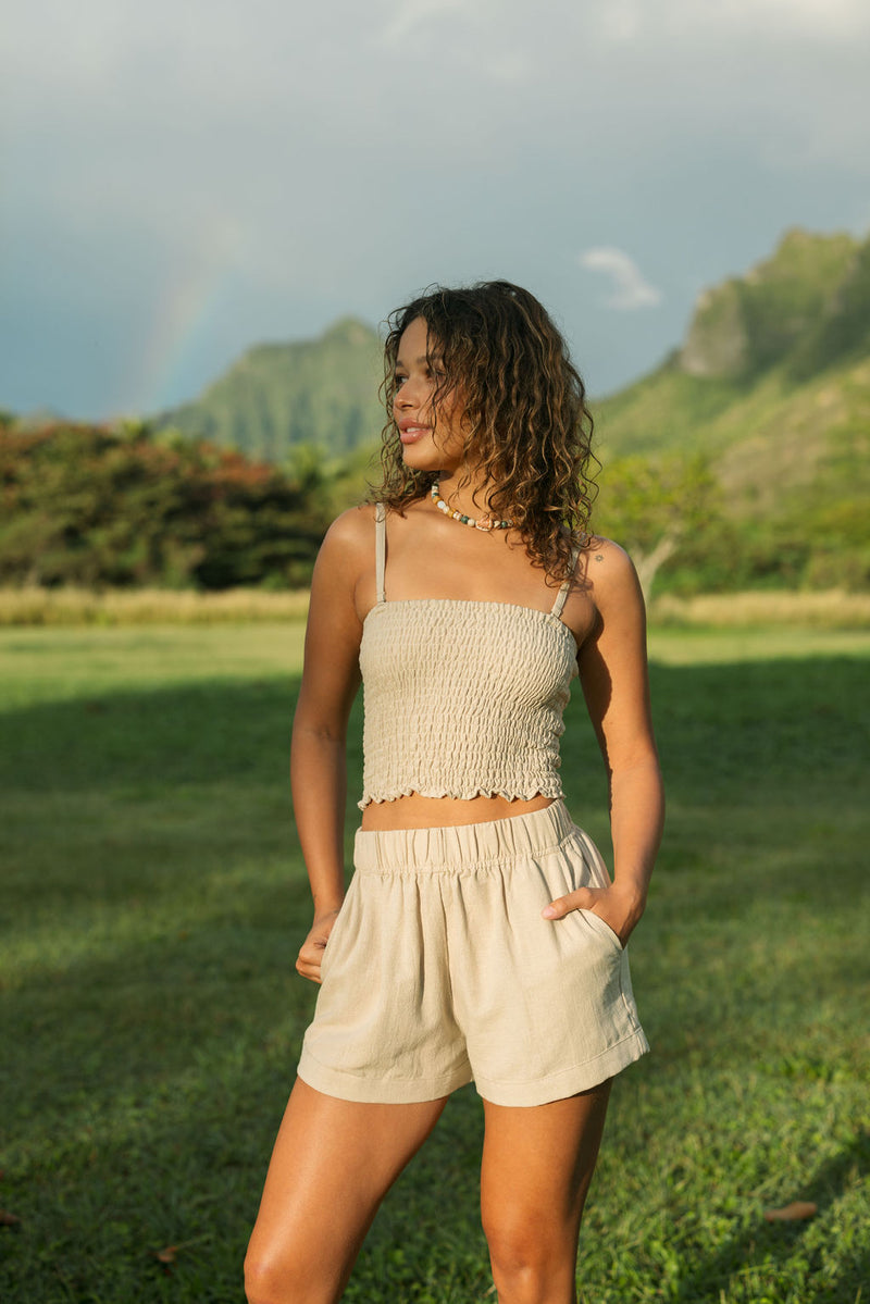 Woman wearing smocked beige linen tube top with spaghetti straps and short.