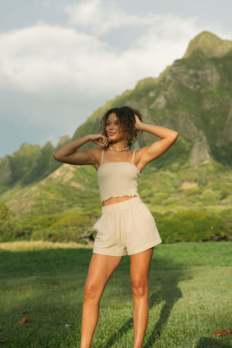 Woman wearing smocked beige linen tube top with spaghetti straps and short.