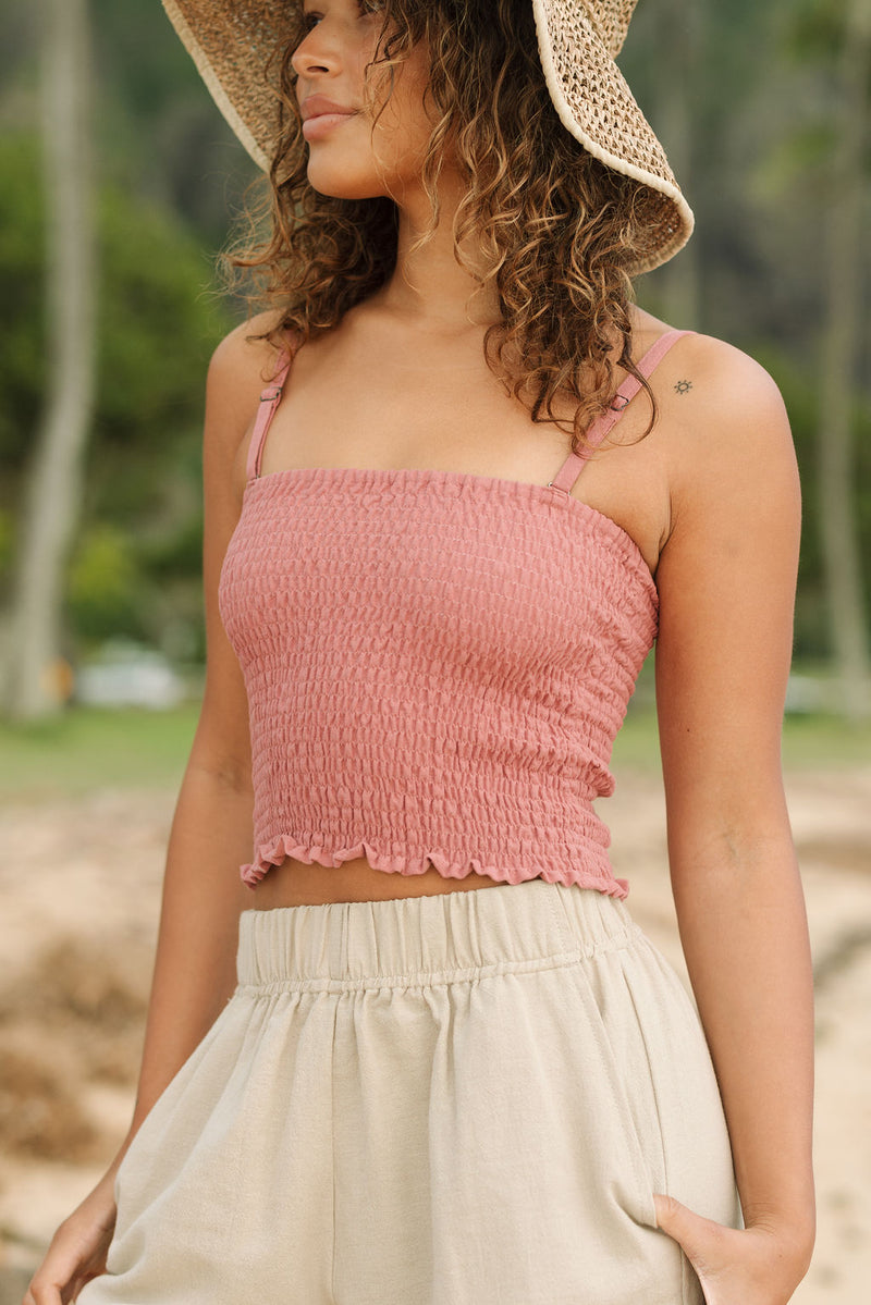 Woman wearing rose linen smocked tube top with spaghetti straps.