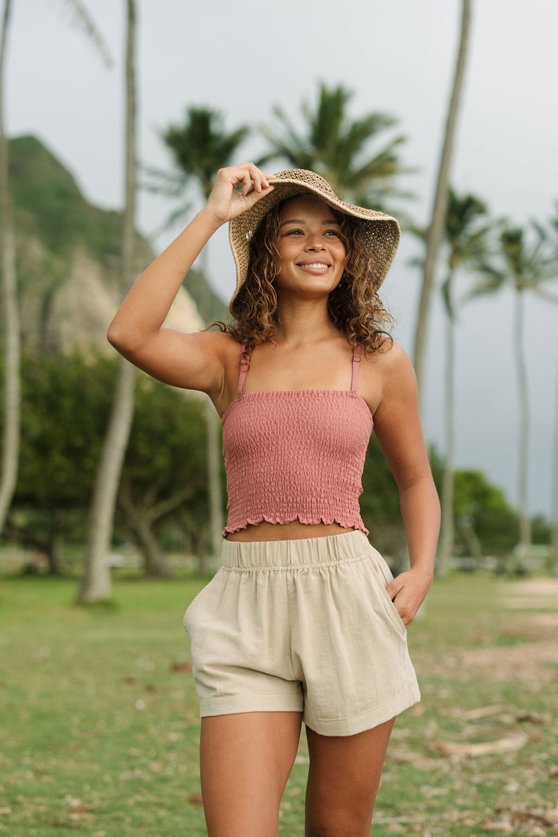 Woman wearing rose linen smocked tube top with spaghetti straps.