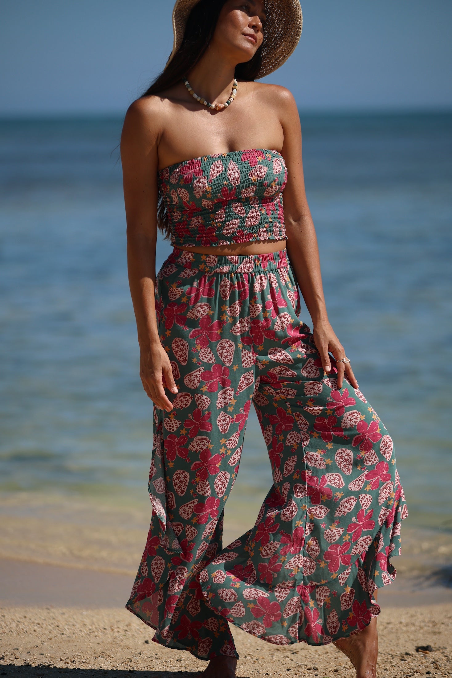 woman with brown hair wearing a teal elastic waist pant with open/slit legs in a shell and pua print