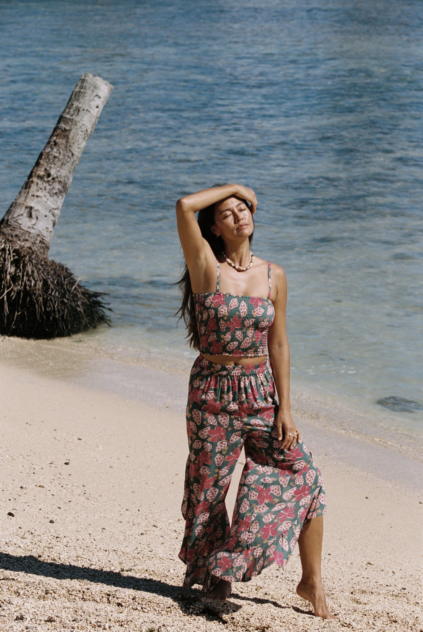 woman with brown hair wearing a teal elastic waist pant with open/slit legs in a shell and pua print