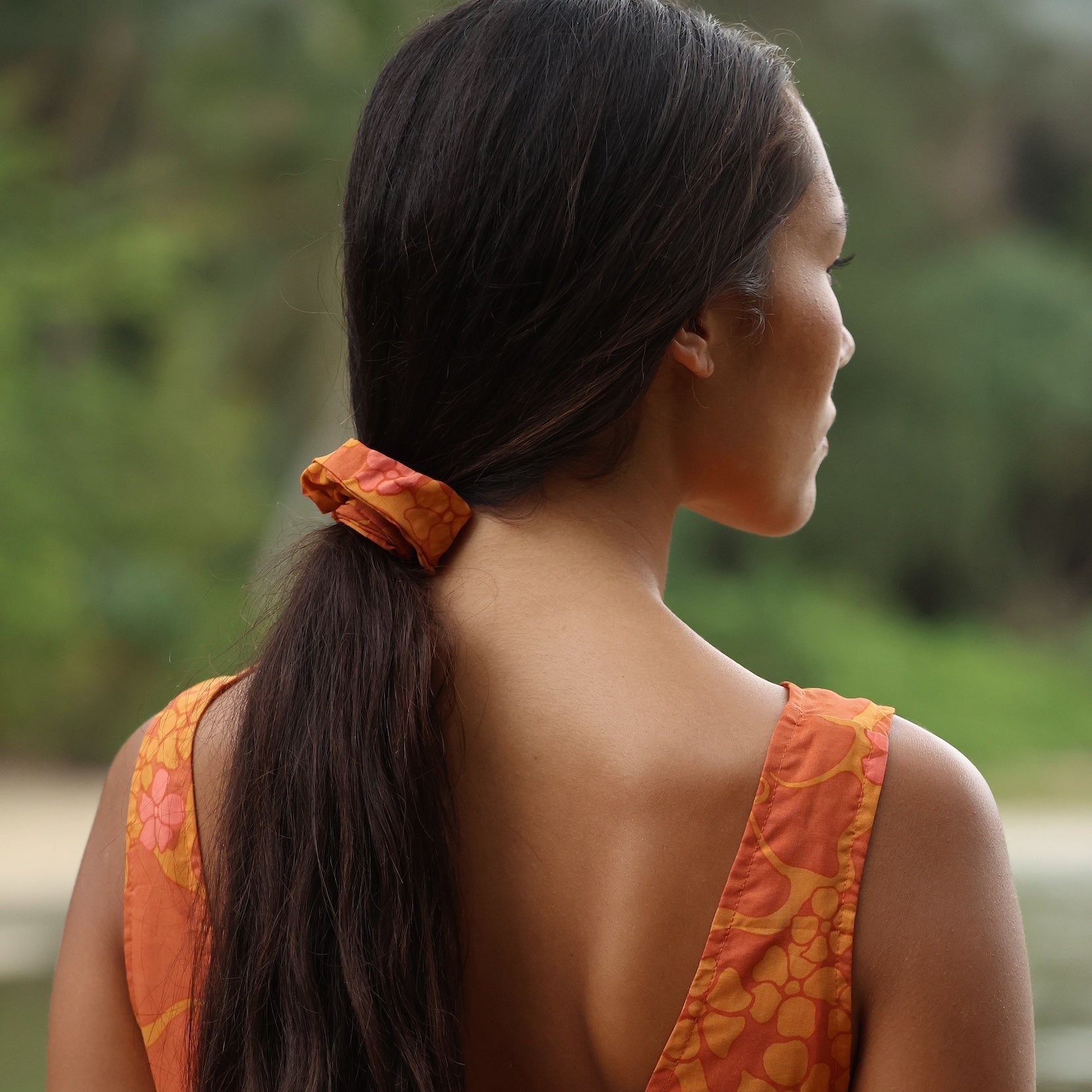 woman with brown hair wearing orange puakenikeni scrunchie