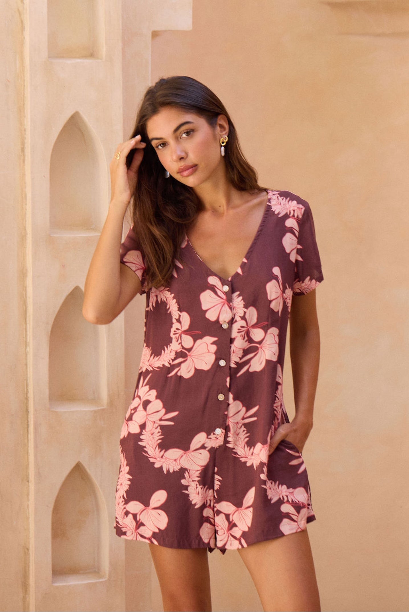 woman with brown hair wearing brown/maroon toned button up romper with pink lei awapuhi print