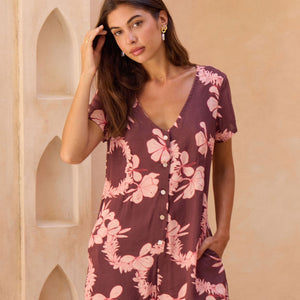 woman with brown hair wearing brown/maroon toned button up romper with pink lei awapuhi print