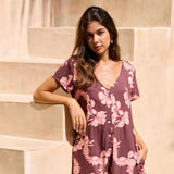 woman with brown hair wearing brown/maroon toned button up romper with pink lei awapuhi print