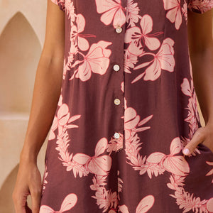 woman with brown hair wearing brown/maroon toned button up romper with pink lei awapuhi print