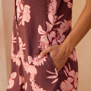 woman with brown hair wearing brown/maroon toned button up romper with pink lei awapuhi print