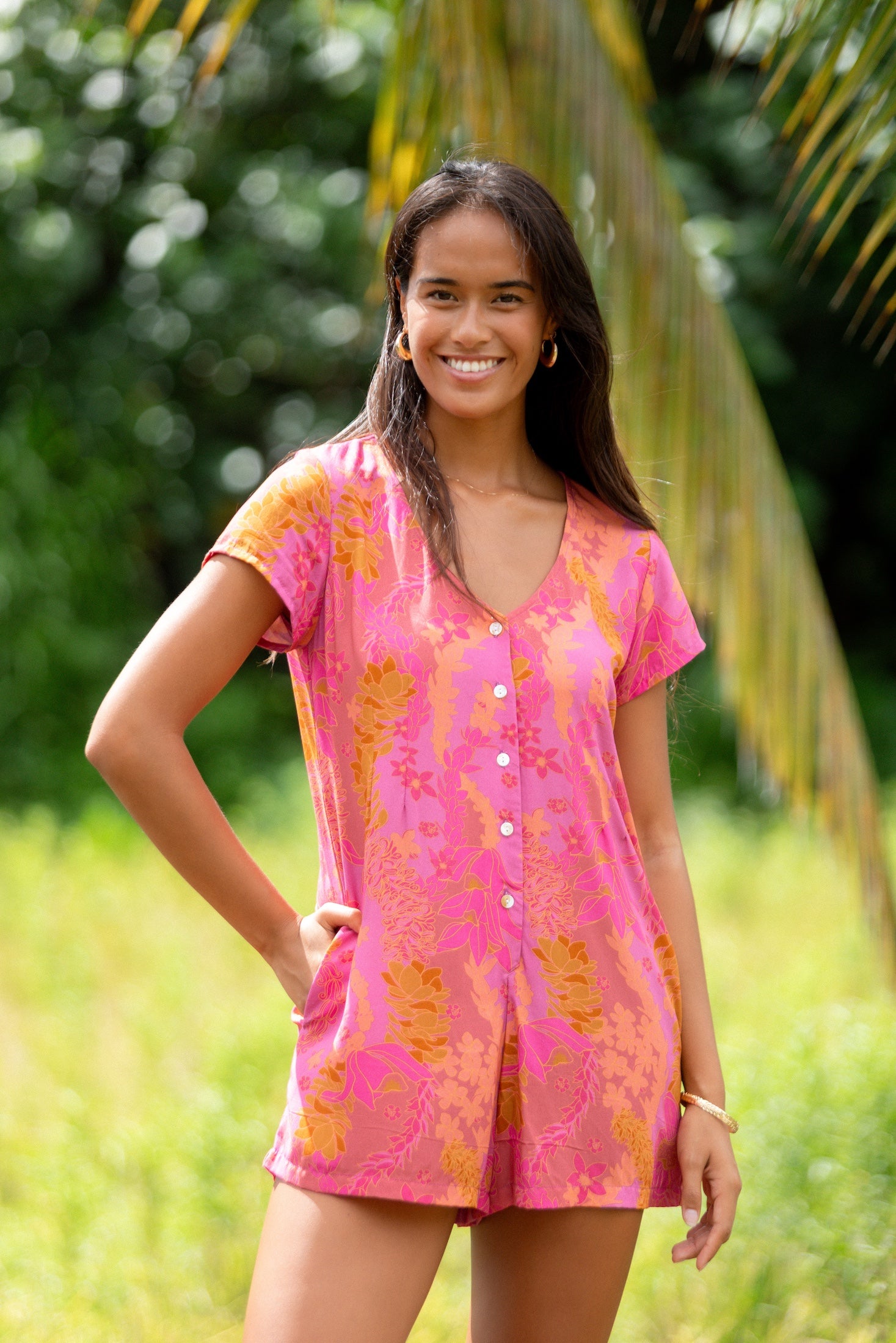 woman wearing a pink button up romper with sleeves with lei print