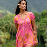 woman wearing a pink button up romper with sleeves with lei print