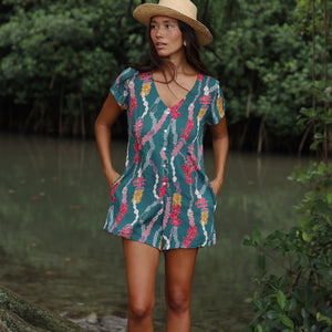 woman with dark brown hair wearing button up romper in dark teal with shell and lei print