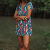 woman with dark brown hair wearing button up romper in dark teal with shell and lei print