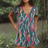 woman with dark brown hair wearing button up romper in dark teal with shell and lei print