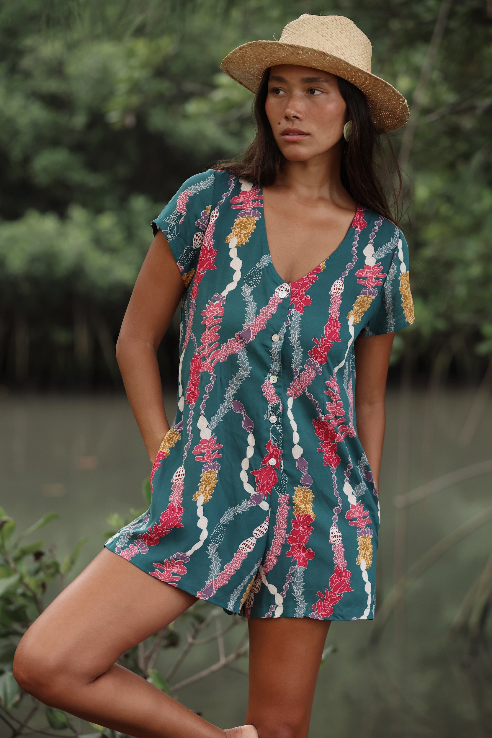 woman with dark brown hair wearing button up romper in dark teal with shell and lei print