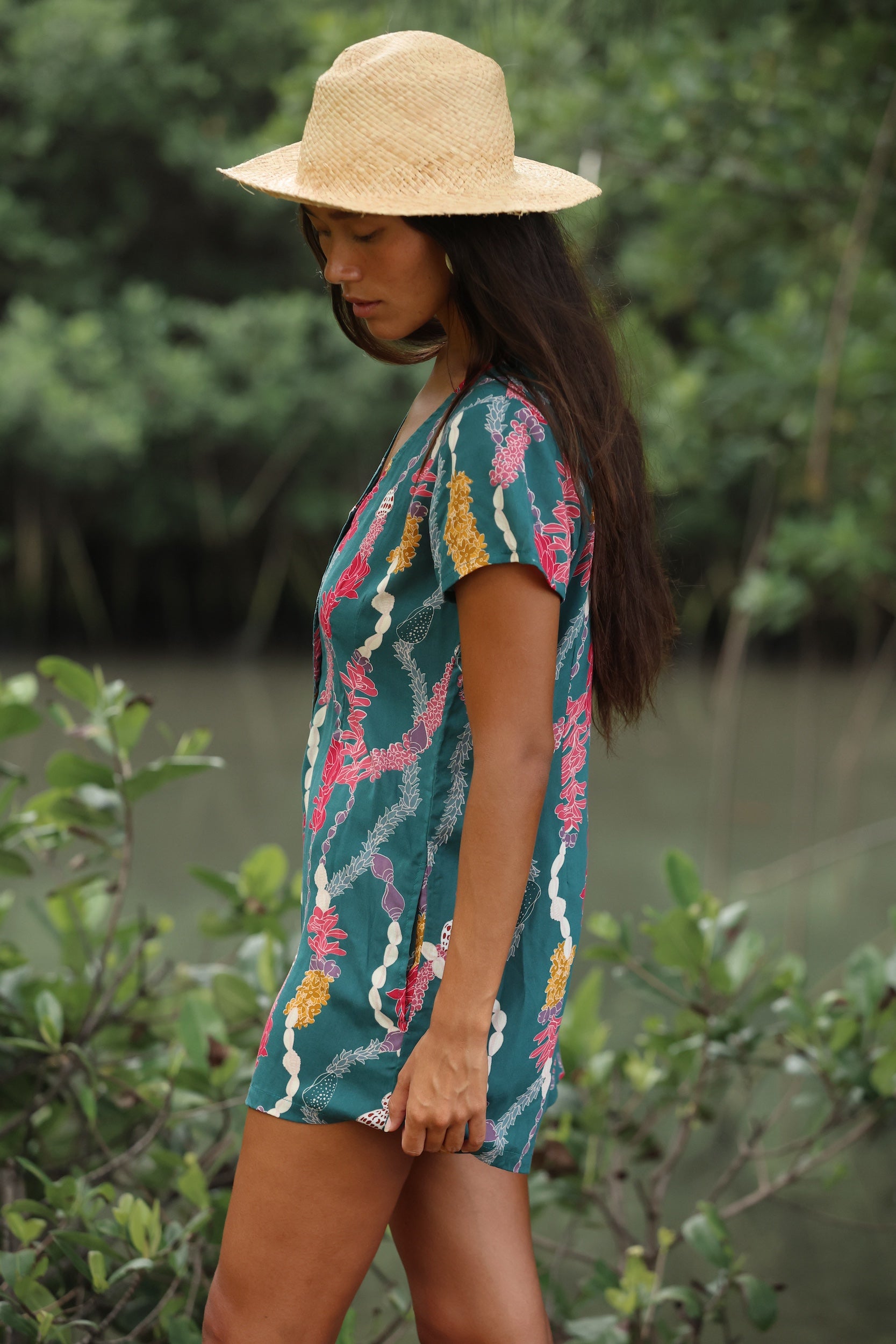 woman with dark brown hair wearing button up romper in dark teal with shell and lei print