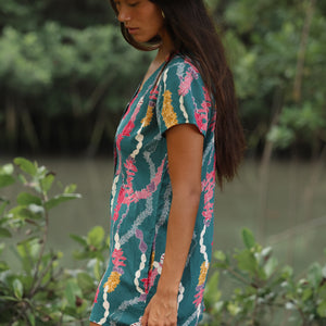 woman with dark brown hair wearing button up romper in dark teal with shell and lei print