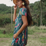woman with dark brown hair wearing button up romper in dark teal with shell and lei print