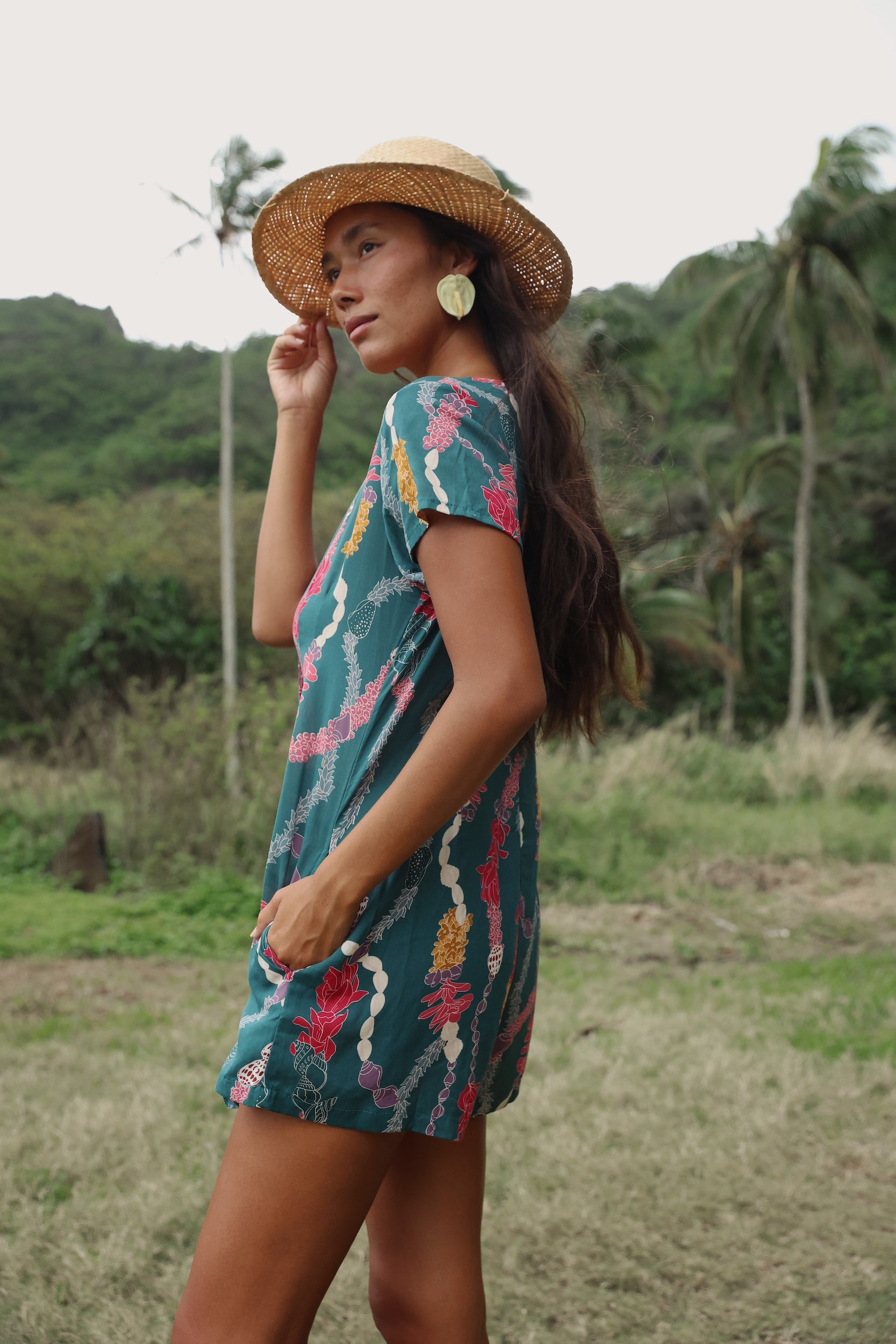 woman with dark brown hair wearing button up romper in dark teal with shell and lei print