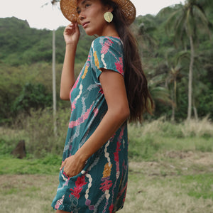 woman with dark brown hair wearing button up romper in dark teal with shell and lei print