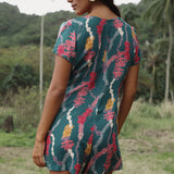 woman with dark brown hair wearing button up romper in dark teal with shell and lei print