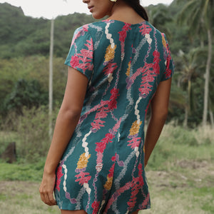 woman with dark brown hair wearing button up romper in dark teal with shell and lei print