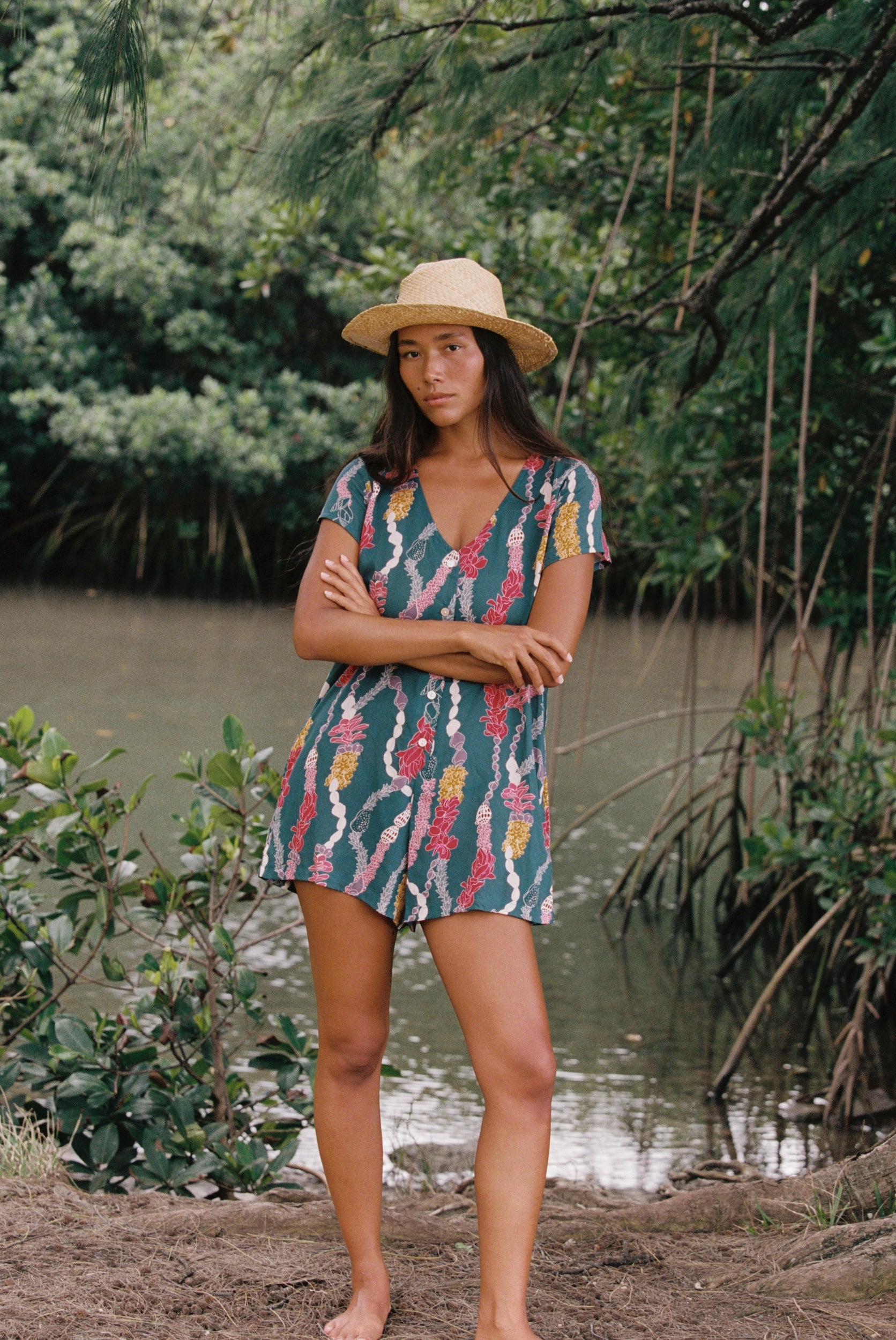 woman with dark brown hair wearing button up romper in dark teal with shell and lei print