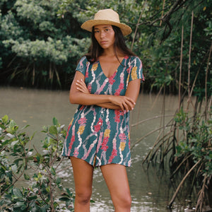 woman with dark brown hair wearing button up romper in dark teal with shell and lei print
