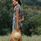 woman with dark brown hair wearing button up romper in dark teal with shell and lei print