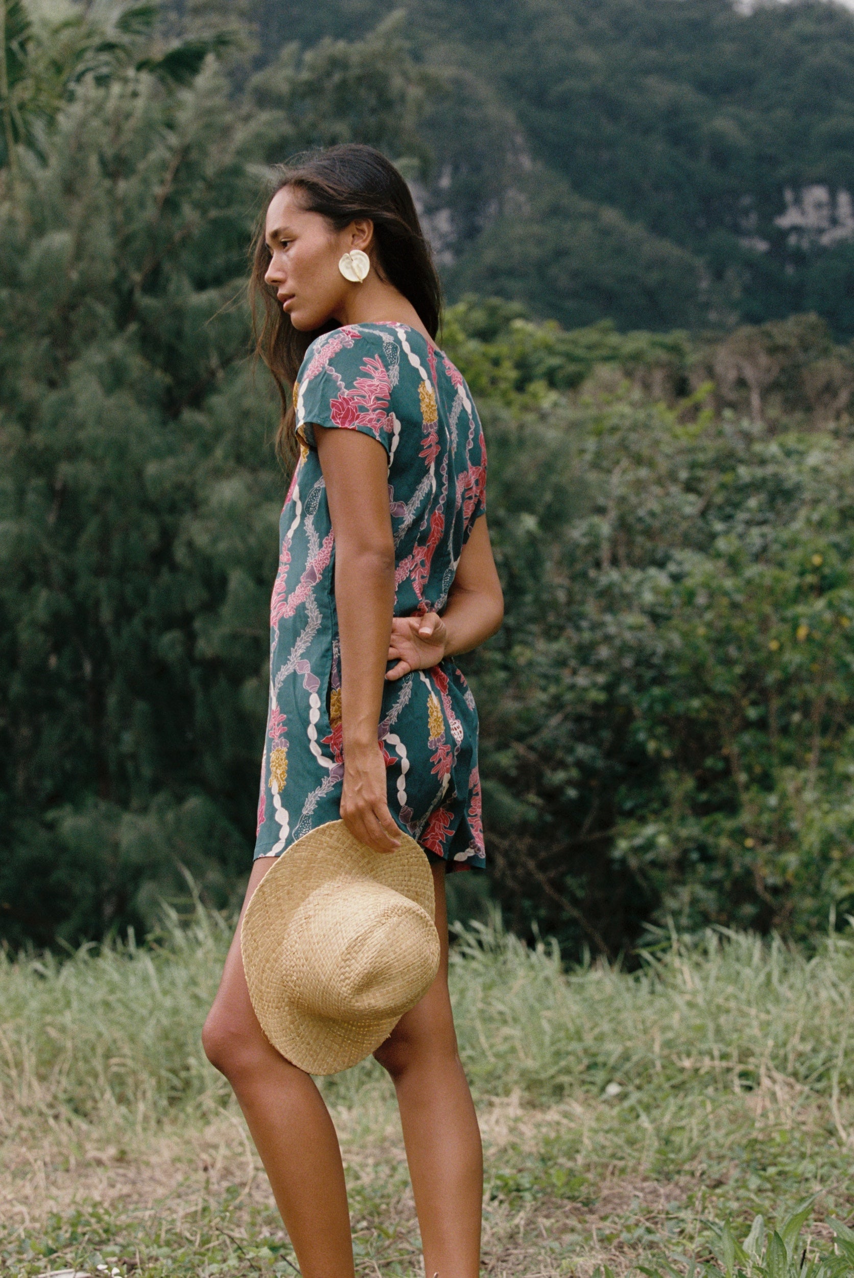 woman with dark brown hair wearing button up romper in dark teal with shell and lei print