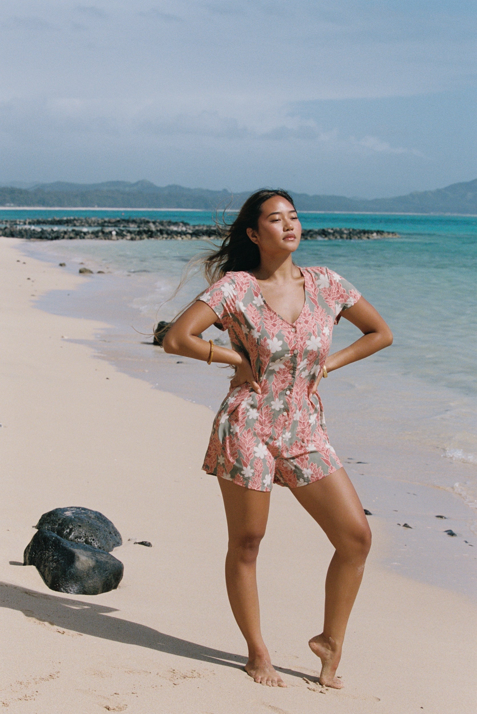woman with brown hair wearing a jade colored button up romper with tiare ginger print