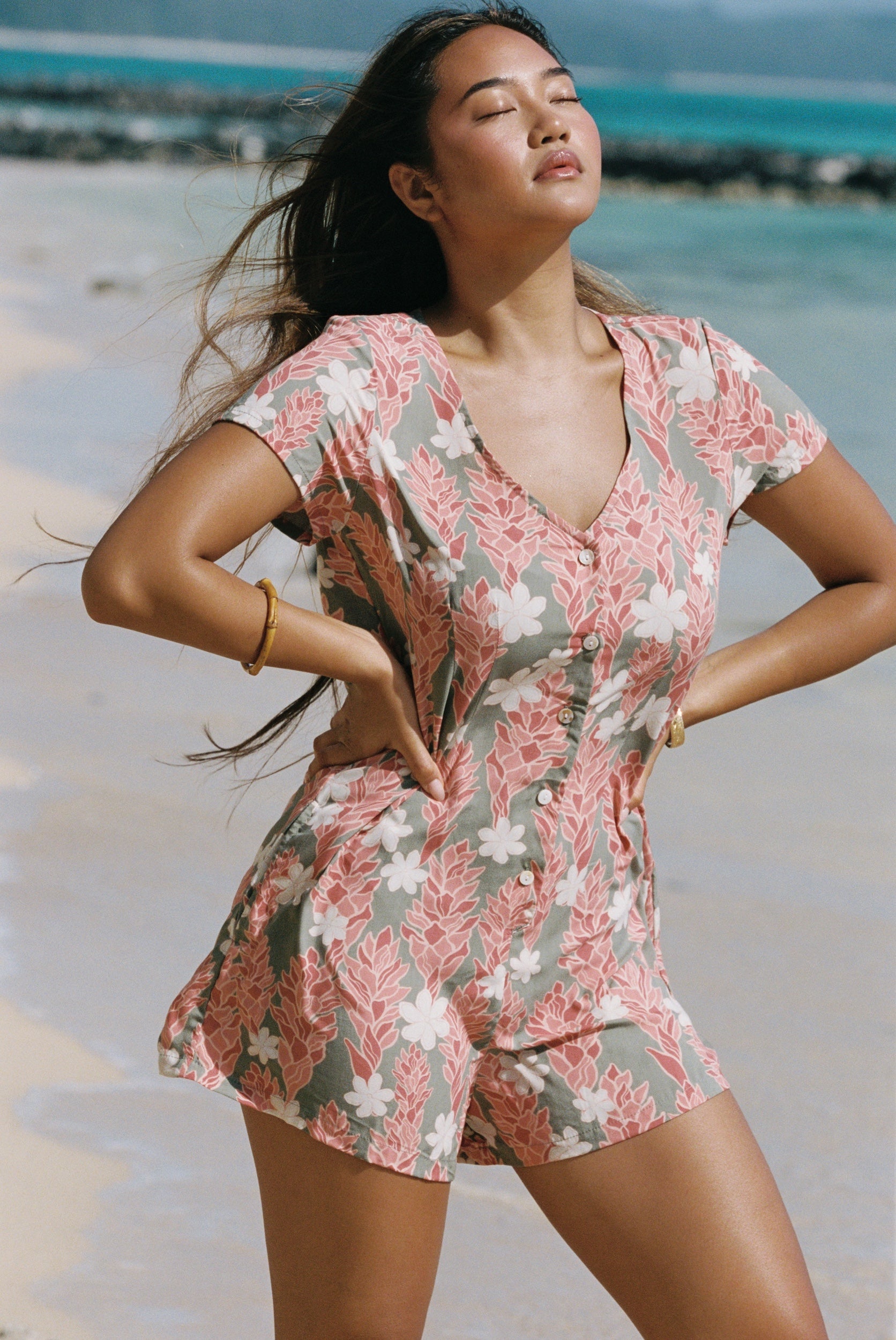 woman with brown hair wearing a jade colored button up romper with tiare ginger print