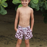 little boy wearing board shorts  in blush and brown hibiscus print.
