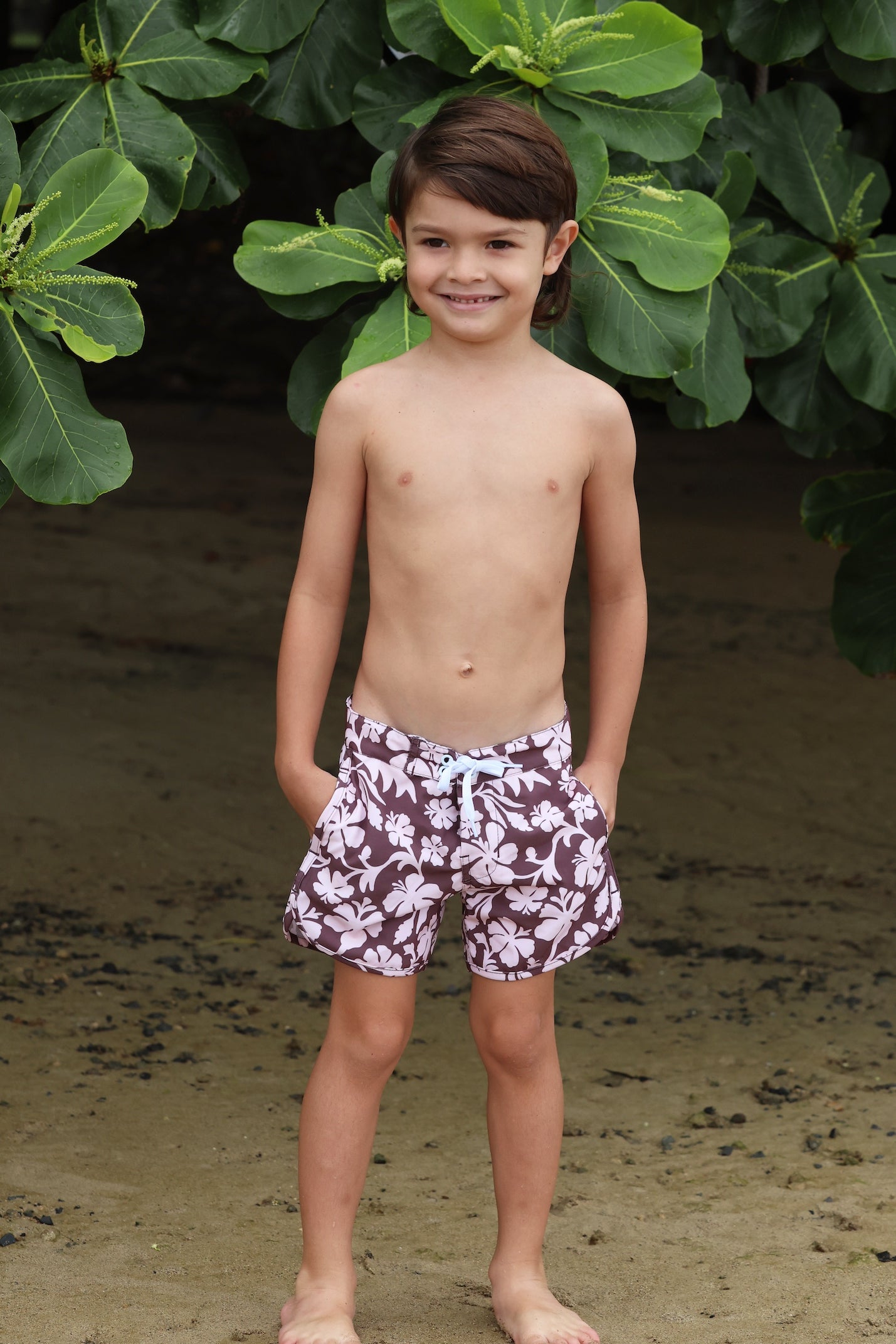 little boy wearing board shorts  in blush and brown hibiscus print.
