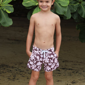 little boy wearing board shorts  in blush and brown hibiscus print.