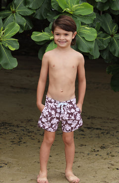 little boy wearing board shorts  in blush and brown hibiscus print.
