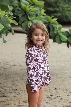little girl wearing long sleeve one piece bikini in blush and brown hibiscus print.
