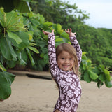 little girl wearing long sleeve one piece bikini in blush and brown hibiscus print.