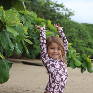 little girl wearing long sleeve one piece bikini in blush and brown hibiscus print.