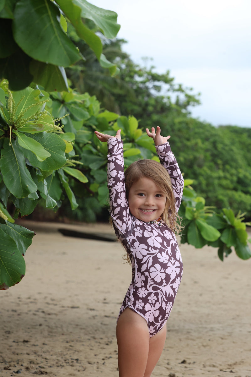 little girl wearing long sleeve one piece bikini in blush and brown hibiscus print.