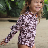 little girl wearing long sleeve one piece bikini in blush and brown hibiscus print.